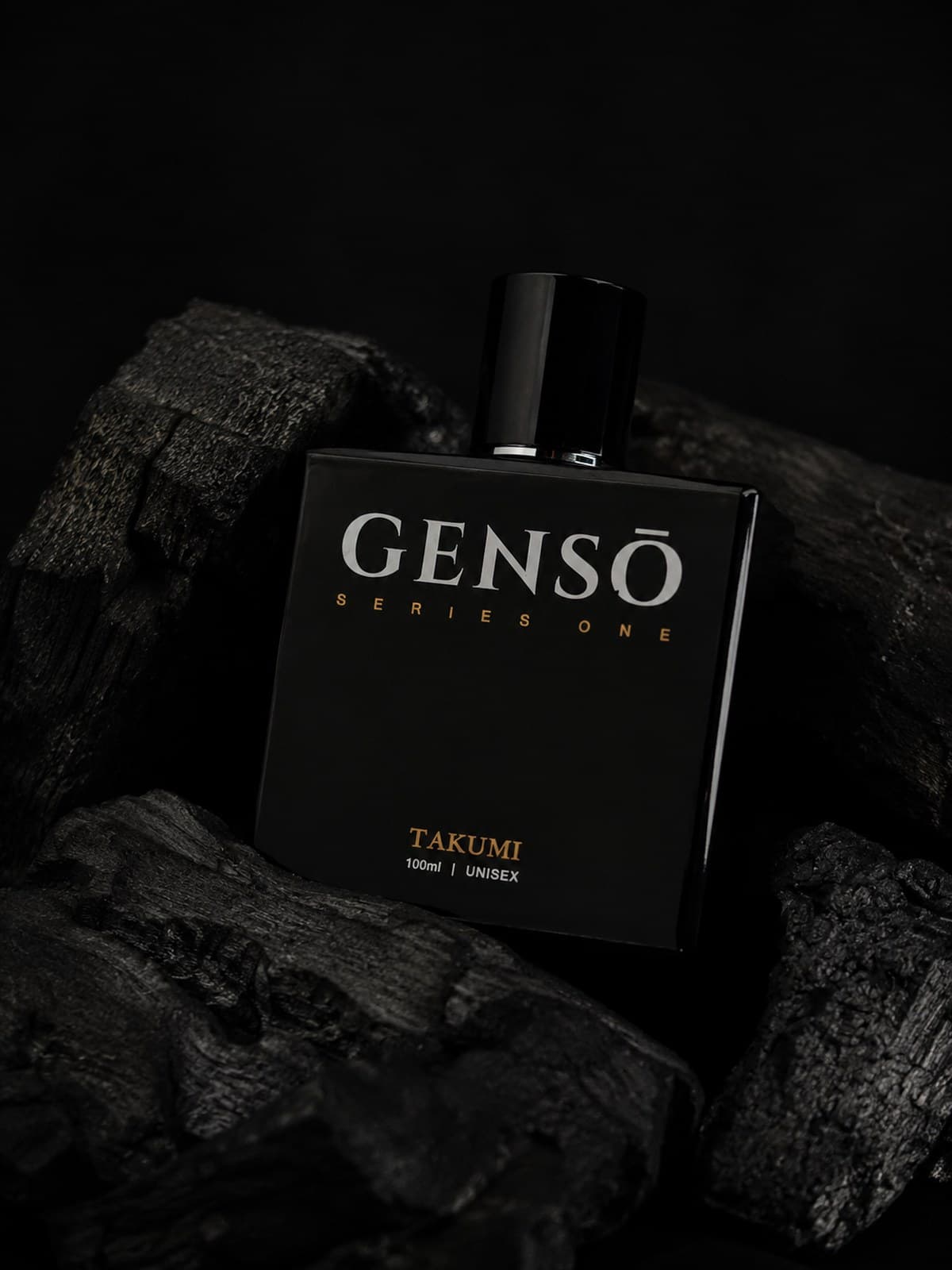 TAKUMI GENSŌ — gloss-black bottle on charcoal, chrome atomizer exposed, GENSŌ wordmark in white and TAKUMI in gold